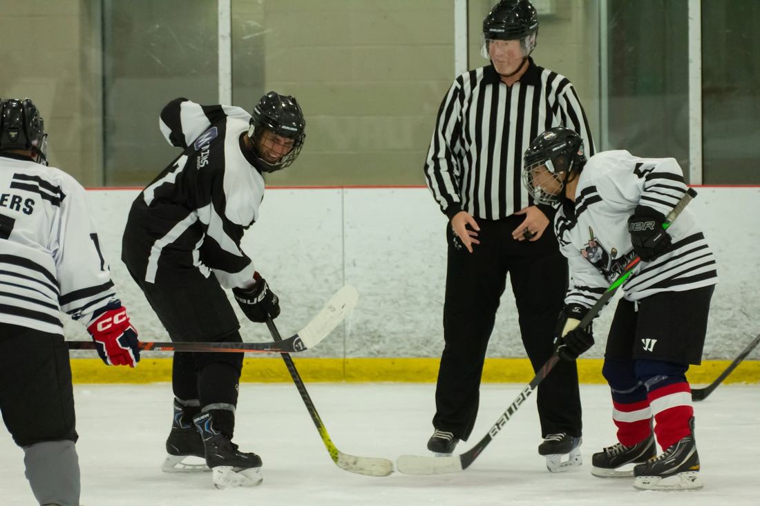 A referee dropping the puck between two players at centre ice