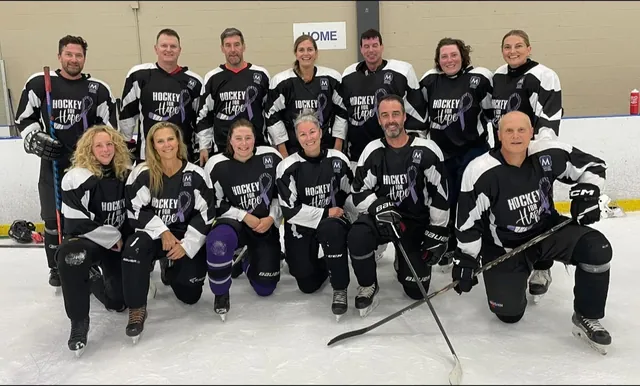 A full team in black and white Hockey for Hope jerseys posing on the ice