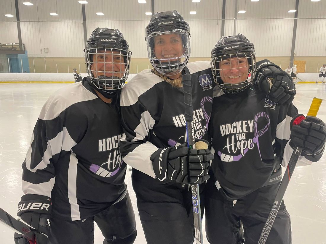 Three Hockey for Hope players in black and purple jerseys standing arm in arm on the ice, smiling