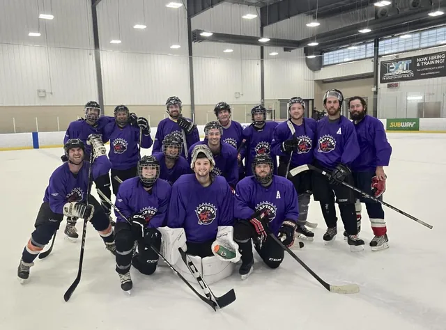 A co-ed team in purple jerseys posing together on the ice after a game