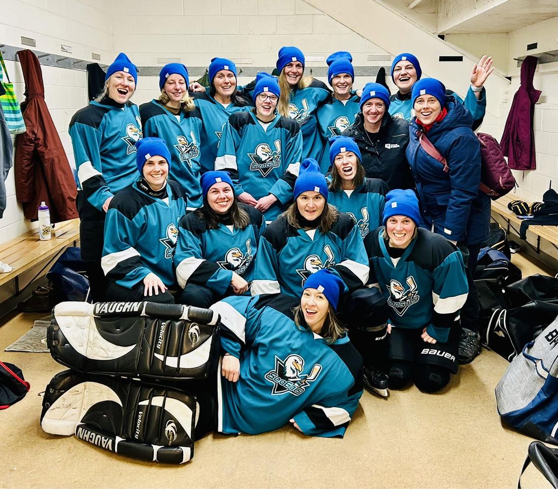 A large team in teal jerseys and toques celebrating together in the dressing room